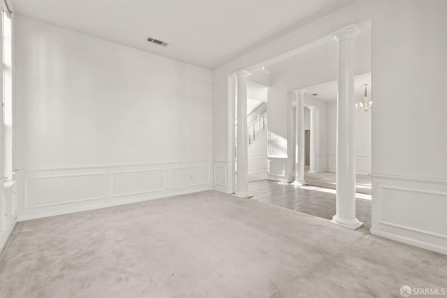 unfurnished room featuring decorative columns, light carpet, and an inviting chandelier