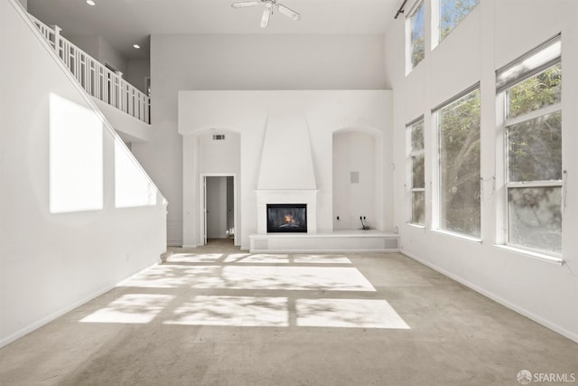 unfurnished living room featuring ceiling fan, light colored carpet, a fireplace, and a high ceiling