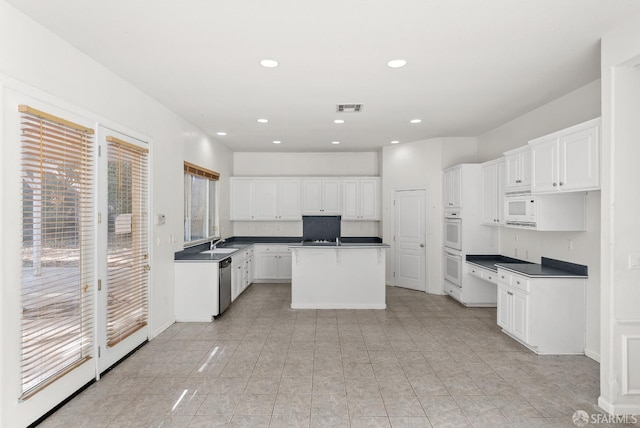 kitchen featuring a center island, white cabinets, sink, stainless steel dishwasher, and light tile patterned flooring