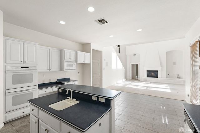 kitchen featuring white appliances, a kitchen island with sink, white cabinets, sink, and a large fireplace