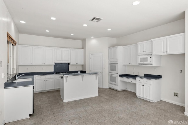 kitchen featuring white appliances, sink, a kitchen island, a kitchen bar, and white cabinetry