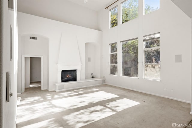 unfurnished living room featuring light carpet, a towering ceiling, and a large fireplace