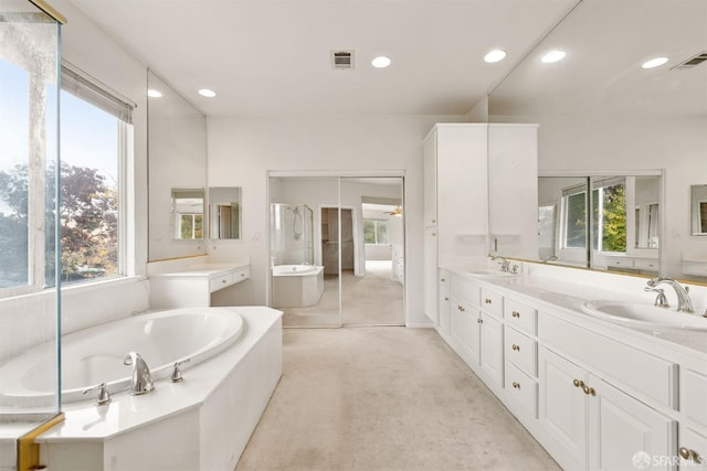 bathroom with plenty of natural light, a relaxing tiled tub, and vanity