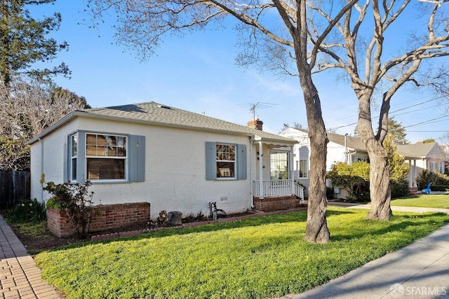 view of front of house featuring a chimney, roof with shingles, fence, a front yard, and stucco siding