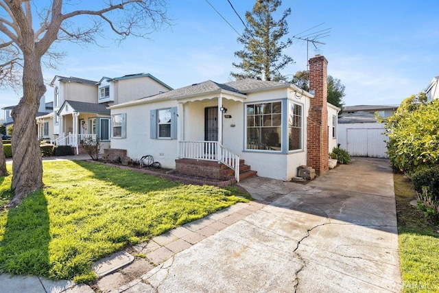 bungalow-style house with a front yard, concrete driveway, a chimney, and stucco siding