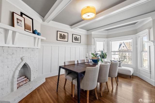 dining area with a brick fireplace, wood-type flooring, ornamental molding, and beamed ceiling