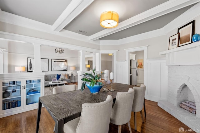 dining room with ornate columns, crown molding, a fireplace, beam ceiling, and dark hardwood / wood-style flooring