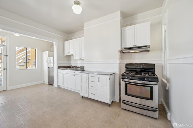 kitchen with baseboards, under cabinet range hood, white cabinets, stainless steel appliances, and a sink