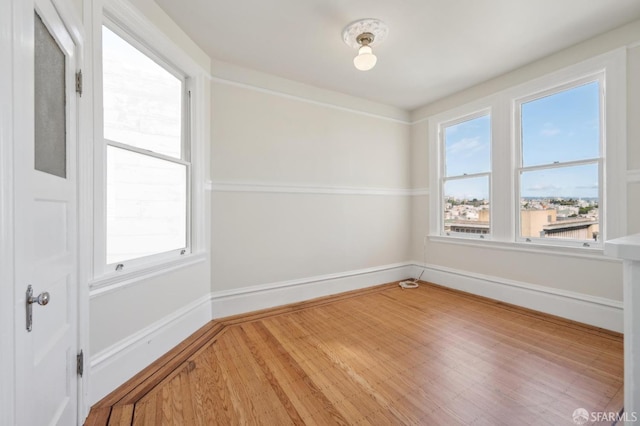 empty room featuring wood finished floors, a healthy amount of sunlight, and baseboards