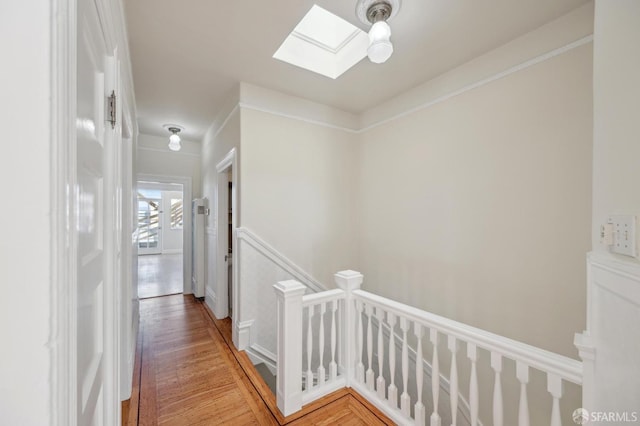 hallway featuring an upstairs landing, light wood finished floors, a skylight, and crown molding