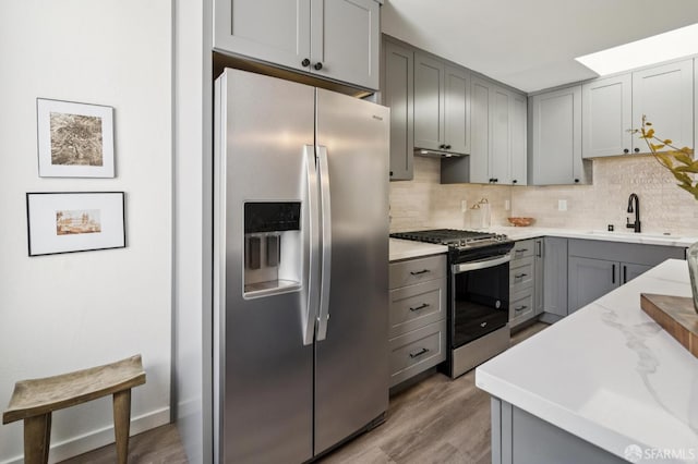 363 Prague St, San Francisco, CA 94112 - kitchen with stainless steel appliances, gray cabinetry, tasteful backsplash, light wood-style flooring, and light stone counters