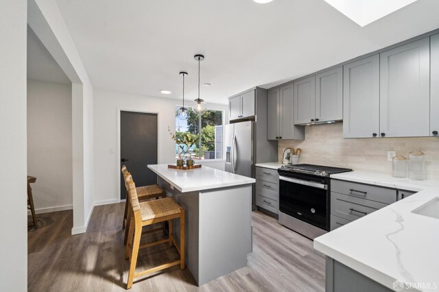 363 Prague St, San Francisco, CA 94112 - kitchen featuring appliances with stainless steel finishes, gray cabinetry, light wood-style floors, tasteful backsplash, and a kitchen bar