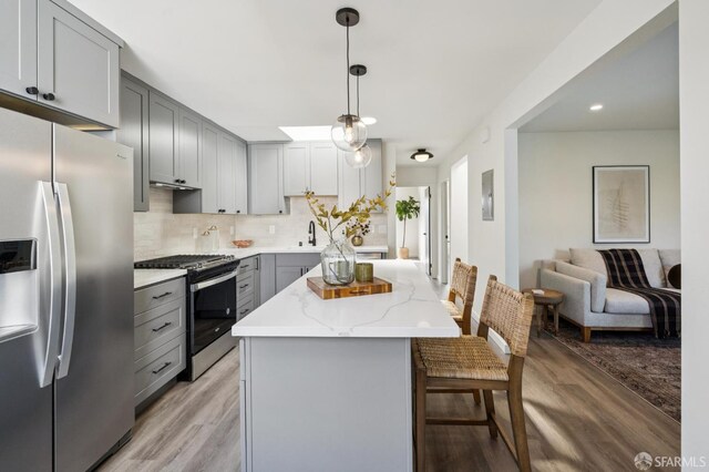 363 Prague St, San Francisco, CA 94112 - kitchen featuring appliances with stainless steel finishes, gray cabinetry, light wood finished floors, a kitchen breakfast bar, and light stone counters