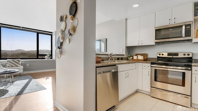 kitchen featuring appliances with stainless steel finishes, a sink, white cabinetry, and baseboards