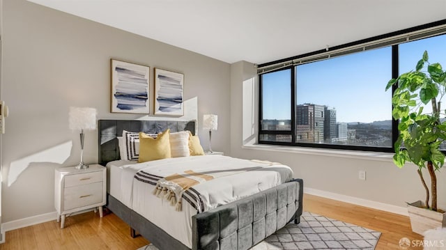 bedroom with baseboards, a city view, and wood finished floors