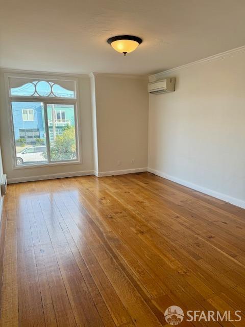 empty room with a wall unit AC, ornamental molding, and wood-type flooring