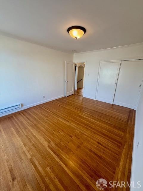 unfurnished bedroom featuring hardwood / wood-style flooring, a closet, and a baseboard heating unit