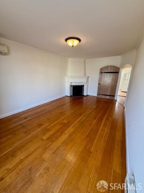 unfurnished living room featuring a wall mounted air conditioner, hardwood / wood-style flooring, and ornamental molding