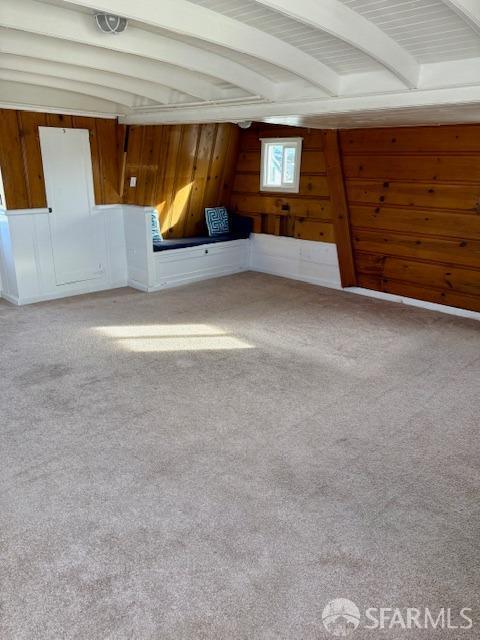 carpeted spare room featuring beam ceiling and wood walls