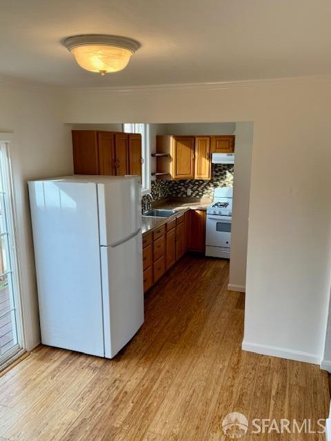 kitchen with sink, white appliances, light hardwood / wood-style floors, and decorative backsplash