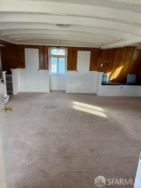 interior space with beam ceiling, wooden walls, and light colored carpet