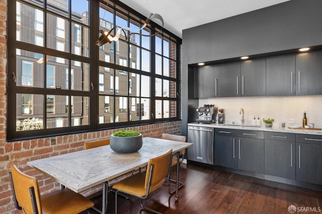 kitchen featuring brick wall, dishwasher, sink, backsplash, and dark wood-type flooring