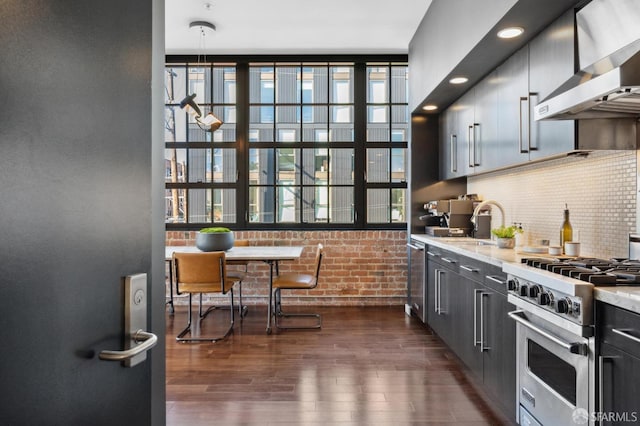 kitchen with wall chimney exhaust hood, tasteful backsplash, appliances with stainless steel finishes, dark hardwood / wood-style floors, and brick wall