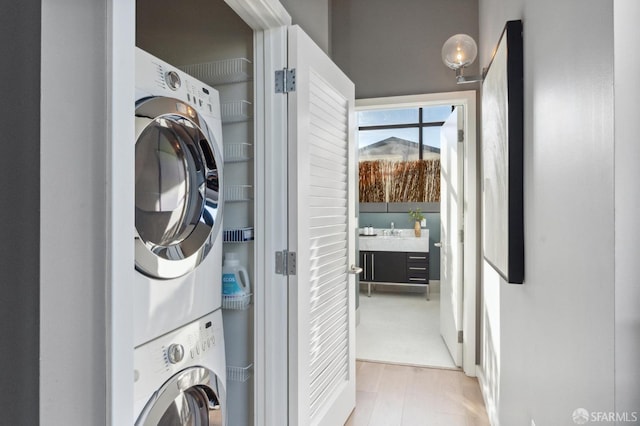 laundry area featuring stacked washer and dryer, sink, and light wood-type flooring