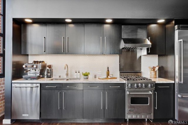 kitchen featuring high end appliances, backsplash, sink, and wall chimney range hood