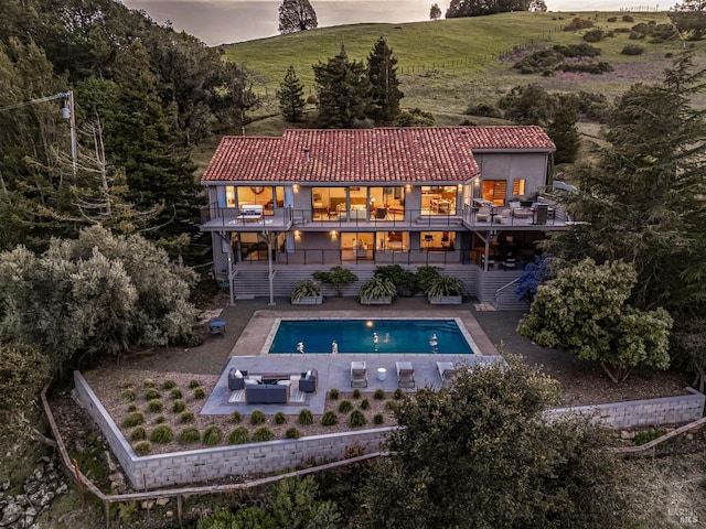 back of property with a tiled roof, stairway, a patio, a balcony, and a fenced in pool