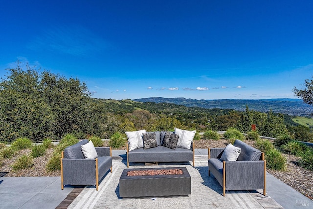 view of patio featuring a forest view, a mountain view, and an outdoor living space with a fire pit