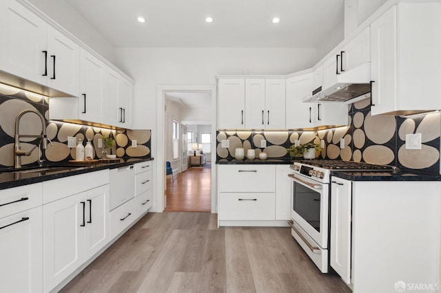 kitchen featuring white range with gas stovetop, under cabinet range hood, dark countertops, light wood-style floors, and decorative backsplash