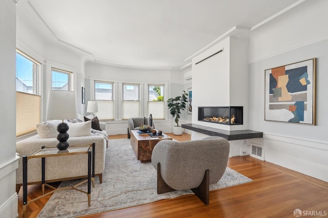 living area featuring wood finished floors, a glass covered fireplace, and crown molding