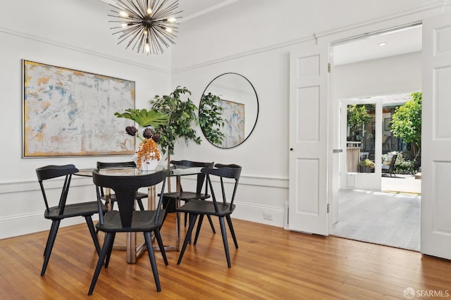 dining space with a chandelier, wood finished floors, a decorative wall, and a wainscoted wall