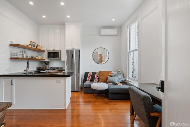 719-721 Shotwell St, San Francisco, CA 94110 - kitchen with stainless steel appliances, a wall mounted air conditioner, dark countertops, white cabinets, and light wood-style floors