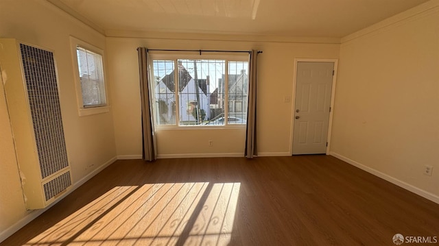 spare room featuring baseboards, wood finished floors, a heating unit, and ornamental molding