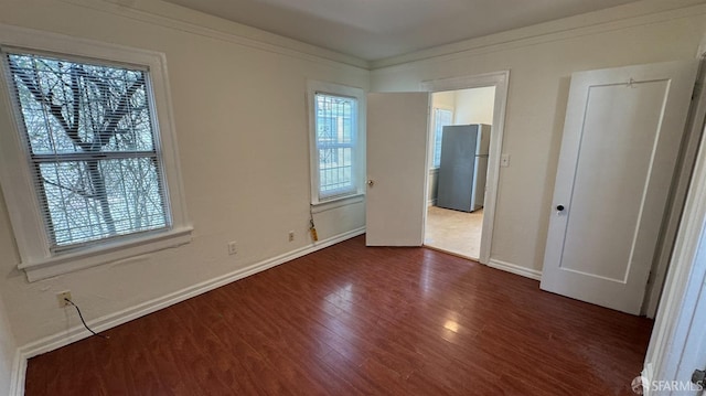 unfurnished bedroom featuring baseboards, dark wood-style floors, ornamental molding, and freestanding refrigerator