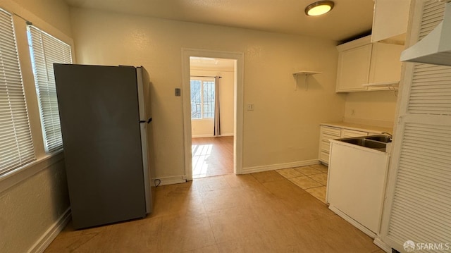 kitchen with a sink, white cabinetry, freestanding refrigerator, light countertops, and baseboards