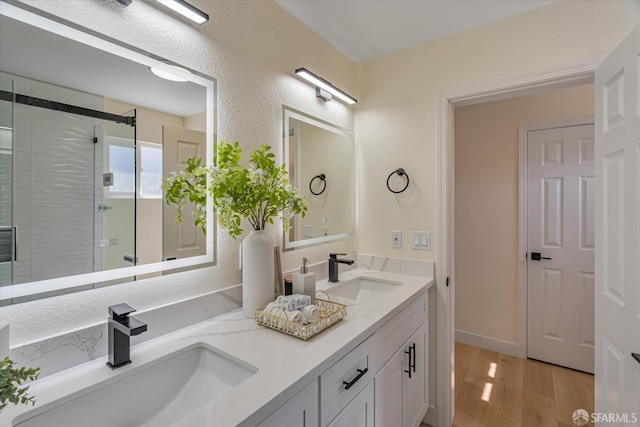 full bath with double vanity, a sink, a shower stall, and wood finished floors