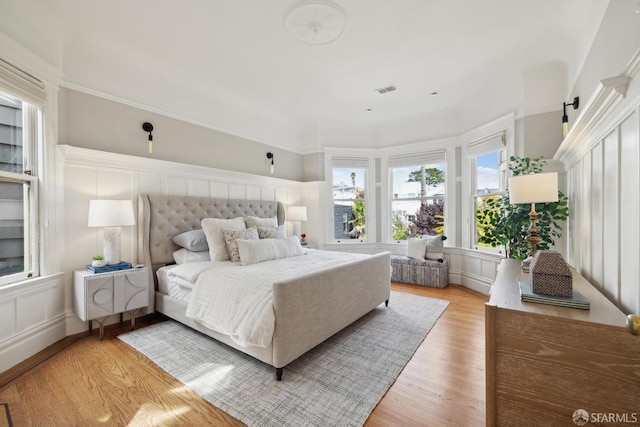 bedroom featuring light wood-type flooring, wainscoting, a decorative wall, and visible vents