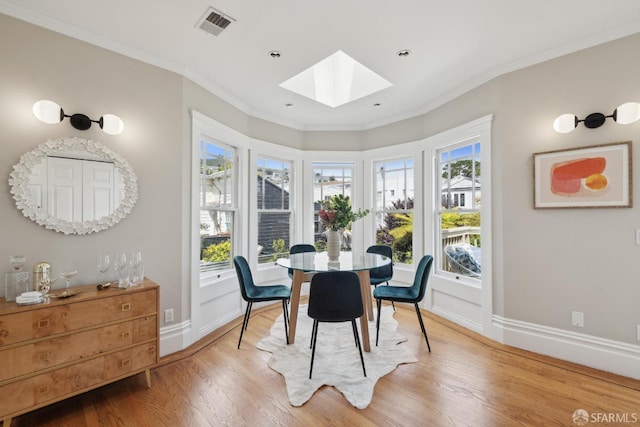 dining area with crown molding, visible vents, baseboards, light wood-type flooring, and a skylight