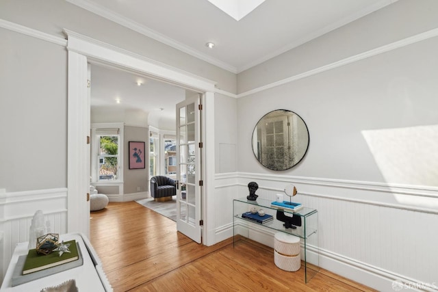 corridor with crown molding, wood finished floors, and a wainscoted wall