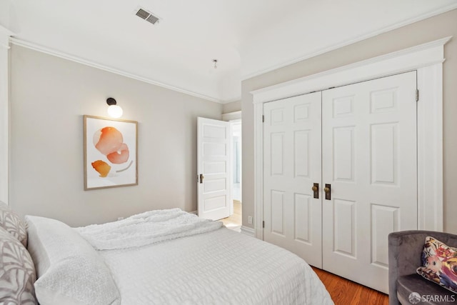 bedroom with ornamental molding, a closet, wood finished floors, and visible vents