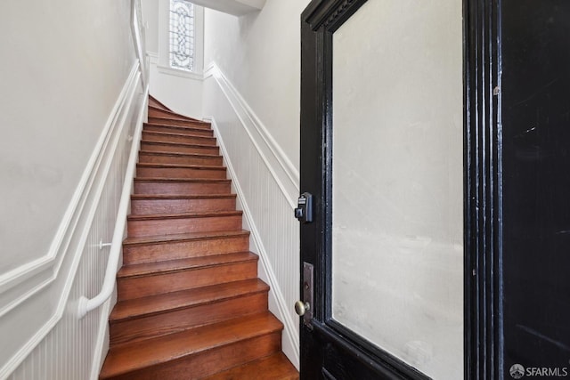 staircase featuring wainscoting and a decorative wall