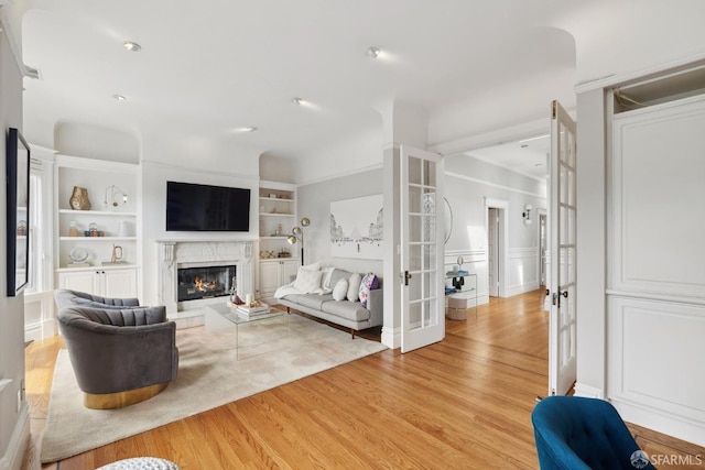 living room with light wood-style floors, built in features, a fireplace, and french doors