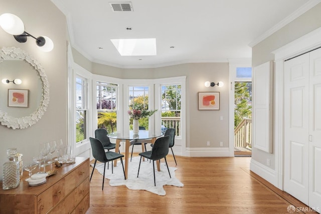 dining area featuring visible vents, crown molding, baseboards, light wood finished floors, and a skylight