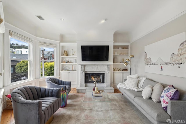 living area with a premium fireplace, built in features, wood finished floors, visible vents, and ornamental molding
