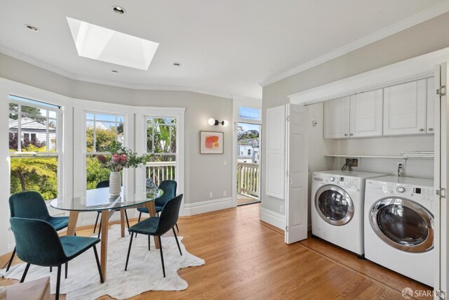 washroom featuring ornamental molding, washer and dryer, cabinet space, light wood-style flooring, and a skylight