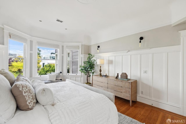 bedroom featuring a wainscoted wall, visible vents, light wood-style flooring, and a decorative wall