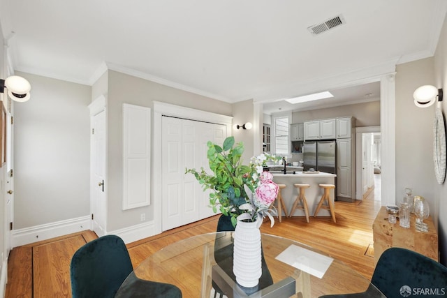 interior space with baseboards, ornamental molding, light wood-type flooring, and visible vents